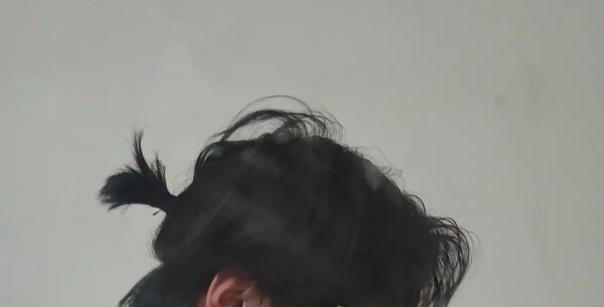 A close-up photo showing the top of a person's hair against a plain wall.