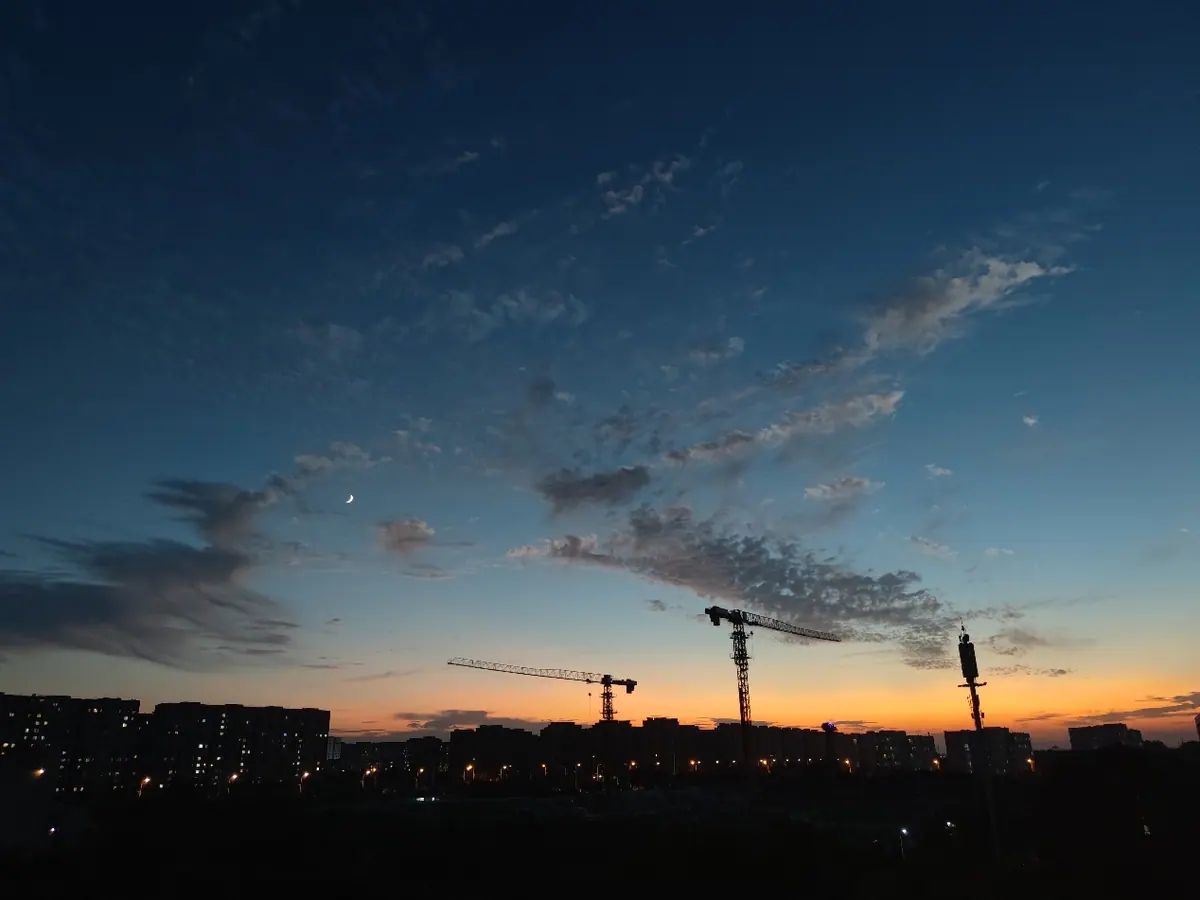 A sunset skyline with cranes and buildings in the distance.